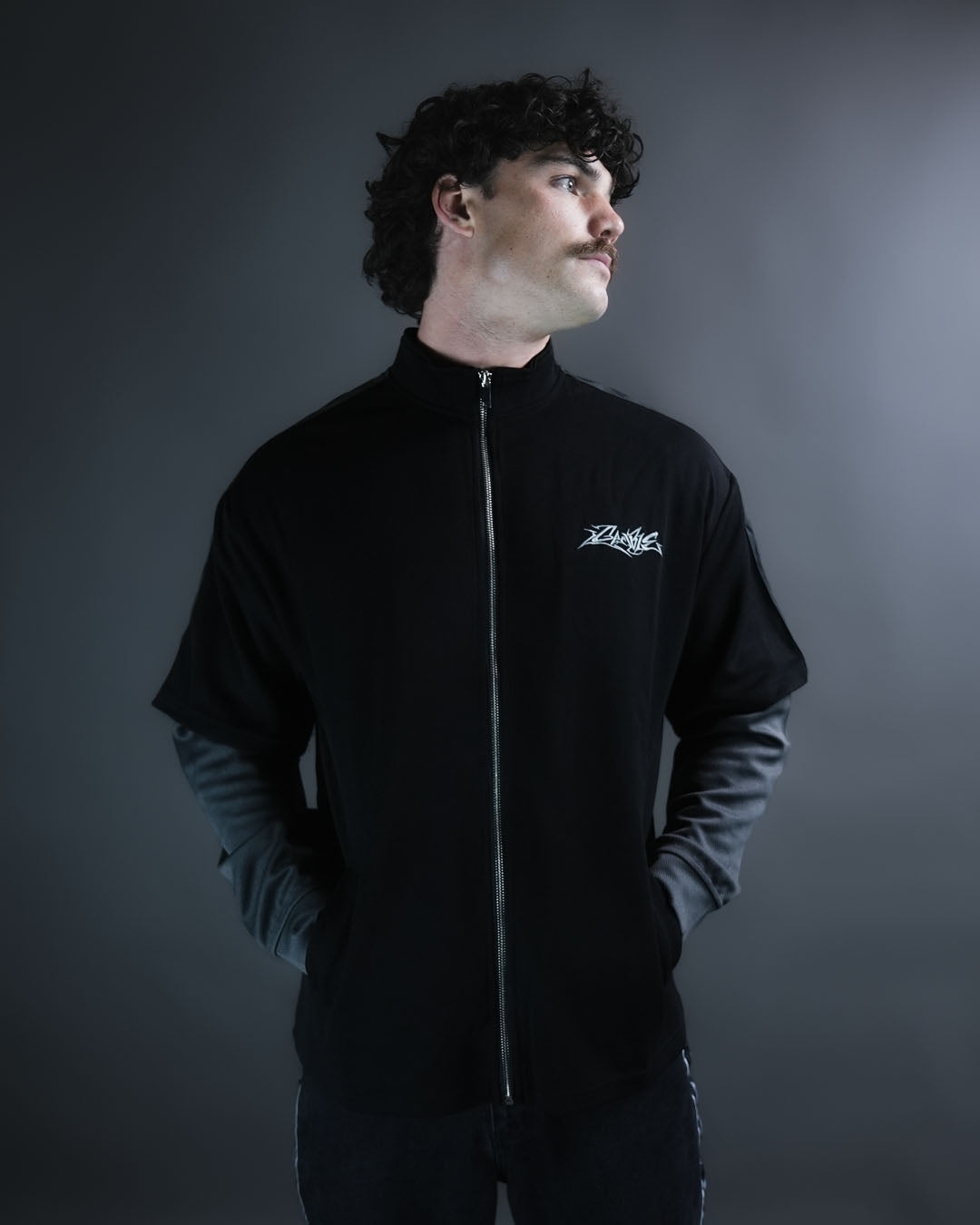 Ace Track Longsleeve front studio portrait showing silver zip, Gamble chest logo and layered charcoal sleeves.