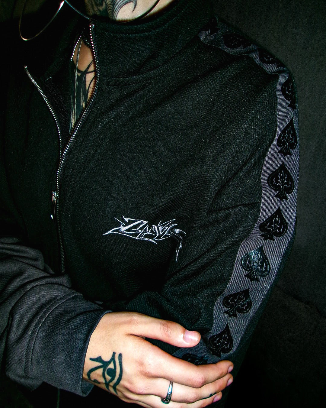 Close-up of Ace Track embroidered chest logo and tonal spade tape down the shoulder.